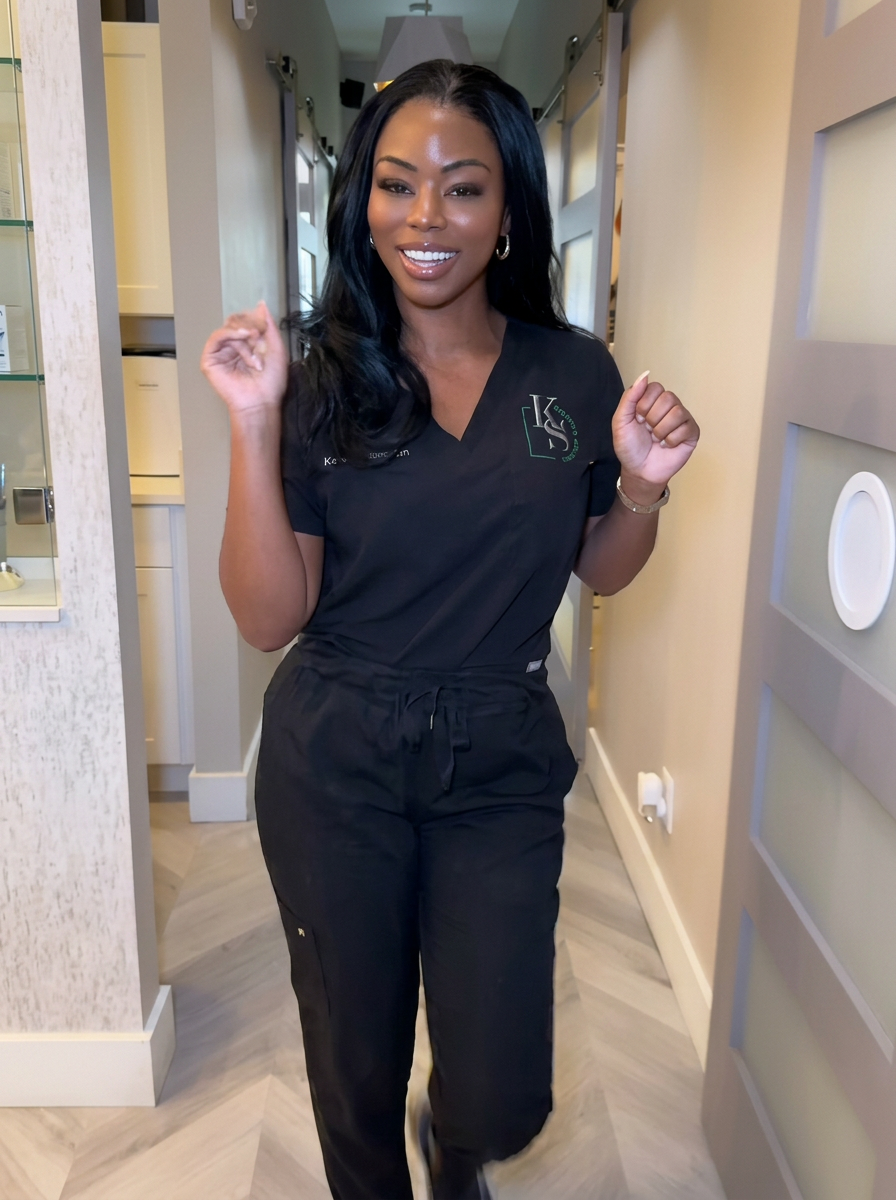 K. Stewart in K Stewart Beauty scrubs smiling in the studio hallway
